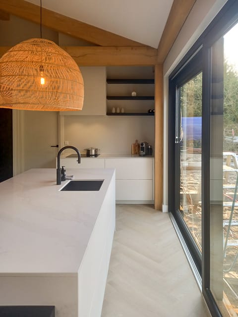 Witte keuken met natuurstenen ombouw en werkblad in een ruimte met houten balken en witte muren