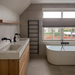 Badkamer Met Natuurstenen Wasbakken, Houten Badmeubel, Zwarte Designradiator En Wit Ligbad