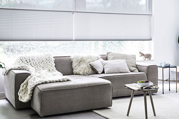 Witte plissé gordijnen in een modern en licht interieur met grijze bank