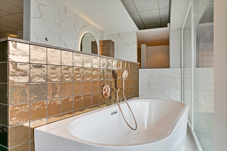 d' Achteromme Nieuwerkerk badkamer met gouden tegels en koperen douchekop